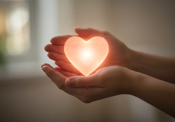 Hands gently holding a glowing heart, symbolizing self-compassion